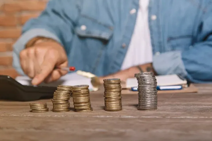 Monedas apiladas en columnas de mayor altura junto a una persona haciendo cuentas