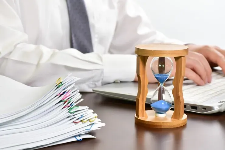 Reloj de arena sobre un escritorio con documentos y un portátil