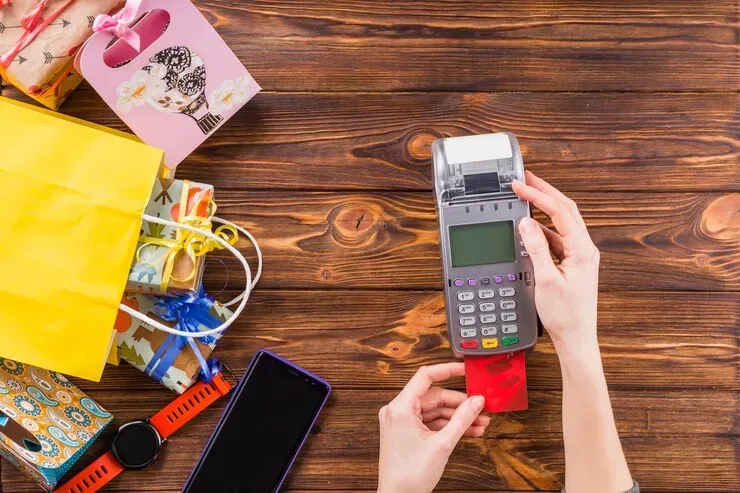 Manos usando un datáfono con una tarjeta, junto a bolsas y regalos de compras