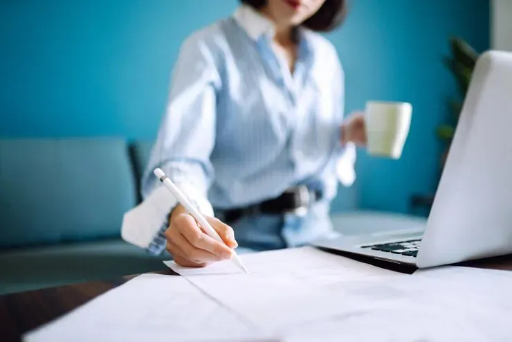 Mujer tomando notas junto a un portátil y una taza de café